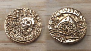 Two-sided bronze coin, one side depicting a skull saying "Sink" and the other side an open-mouthed shark saying "swim"